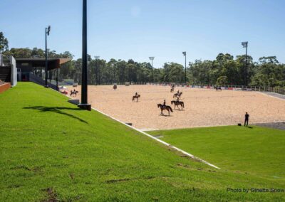 seven Horses being ridden at the Willinga Park show jumping arena with a view of the new grandstand and six new GM Poles sports lighting towers in the background.