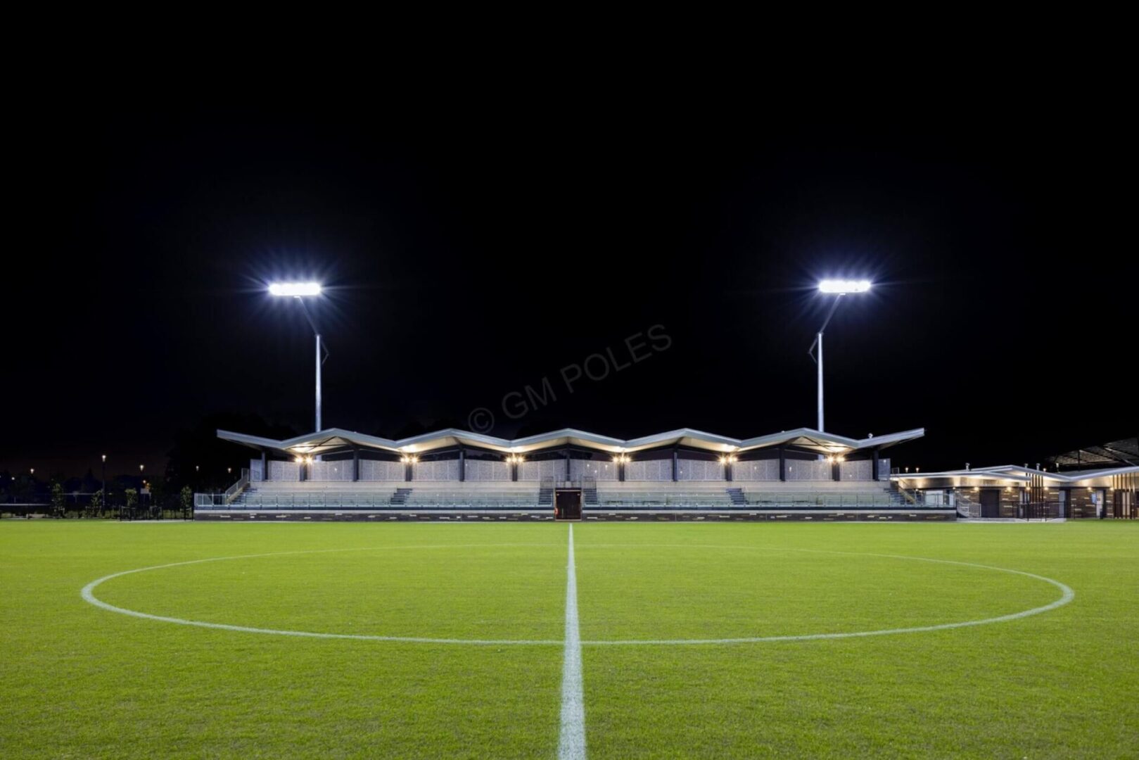 High-quality sports field lighting using tall steel poles illuminating a football field and grandstand at night